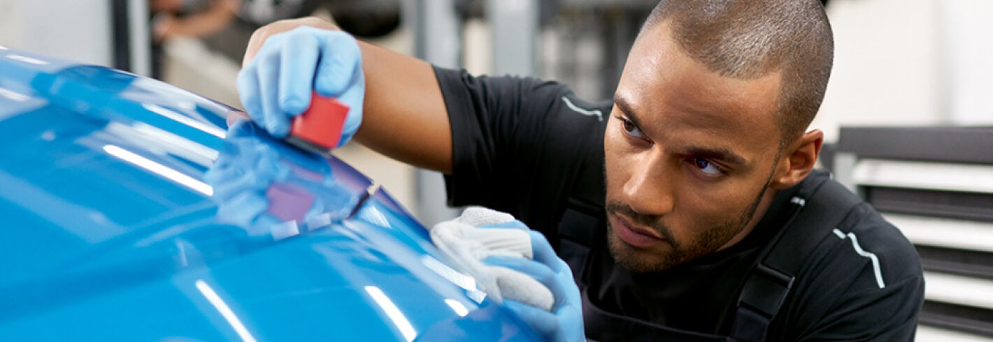 A BMW Certified Technician concentrates intensely while using a small sander to fine-tune a body repair finish.