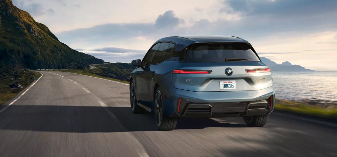 A rear view of a blue BMW iX driving down an oceanside highway