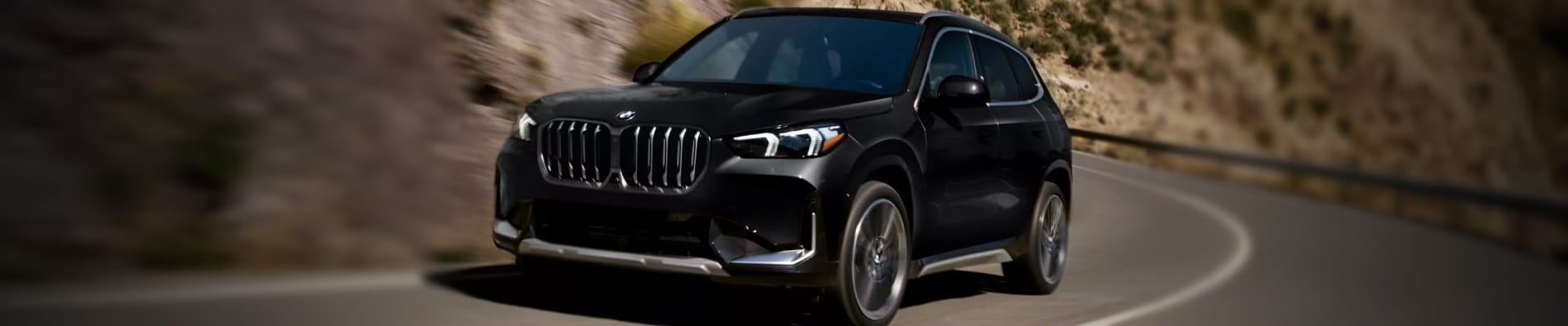 Black BMW SUV driving along a winding mountain road.