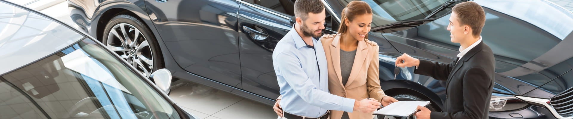 Couple completing paperwork with a sales representative at a car dealership.
